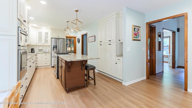 1117 Windreef Cir, Okemos, MI 48864 - kitchen featuring light wood-style flooring, a breakfast bar area, white cabinets, appliances with stainless steel finishes, and light stone countertops