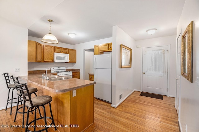 1262 Evans St, Mason, MI 48854 - kitchen with white appliances, a kitchen bar, a peninsula, brown cabinets, and light wood-type flooring