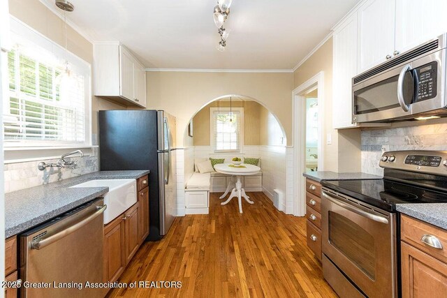 720 N Fairview Ave, Lansing, MI 48912 - kitchen with stainless steel appliances, wood finished floors, white cabinets, ornamental molding, and pendant lighting