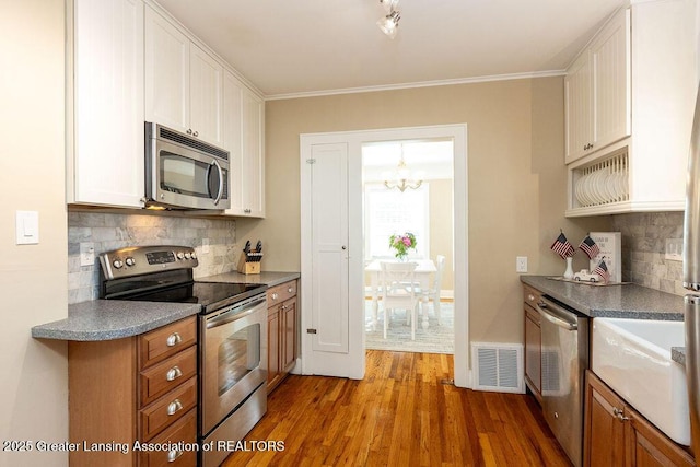 720 N Fairview Ave, Lansing, MI 48912 - kitchen with appliances with stainless steel finishes, backsplash, white cabinetry, wood finished floors, and crown molding