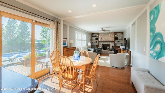 5939 Highgate Ave, East Lansing, MI 48823 - dining area with built in shelves, wood finished floors, a fireplace, a ceiling fan, and crown molding