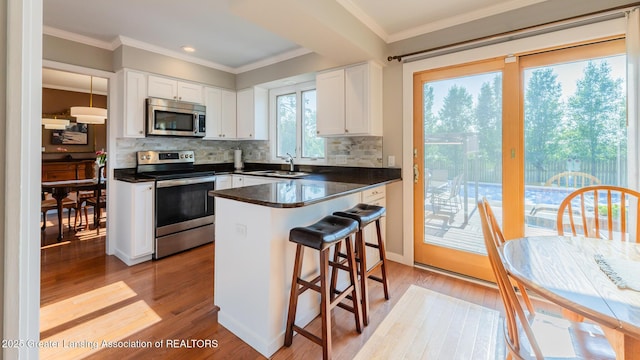 5939 Highgate Ave, East Lansing, MI 48823 - kitchen featuring appliances with stainless steel finishes, dark countertops, light wood-type flooring, white cabinetry, and crown molding