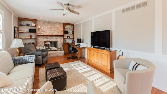 5939 Highgate Ave, East Lansing, MI 48823 - living room featuring built in shelves, light wood-style floors, ceiling fan, a brick fireplace, and a desk