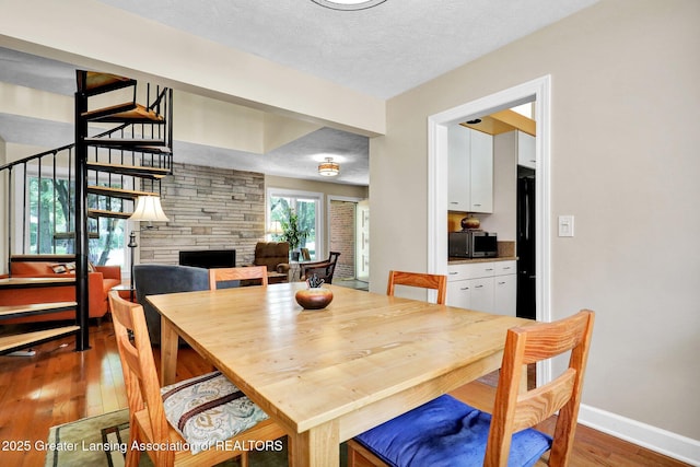 1603 Roseland Ave, East Lansing, MI 48823 - dining area featuring wood-type flooring, a stone fireplace, stairs, and a textured ceiling