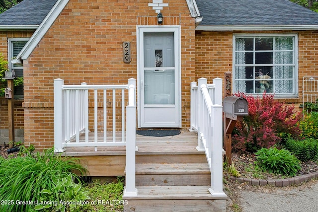 229 Rockingham Ave, Alma, MI 48801 - entrance to property featuring a shingled roof, brick siding, and a wooden deck