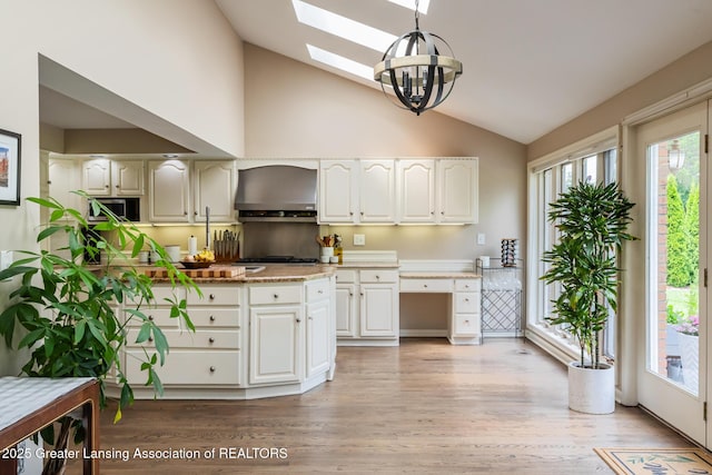 1717 Nottingham Rd, Lansing, MI 48911 - kitchen featuring lofted ceiling, wall chimney exhaust hood, a chandelier, a skylight, and light wood-style floors