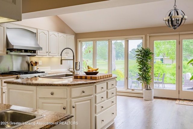 1717 Nottingham Rd, Lansing, MI 48911 - kitchen featuring wall chimney range hood, vaulted ceiling, light wood-style flooring, a kitchen island, and white cabinets