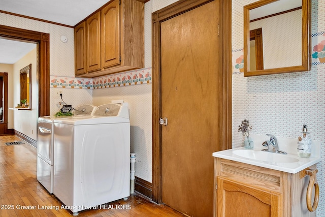301 E Emerson St, Ithaca, MI 48847 - washroom with wallpapered walls, washer and clothes dryer, light wood finished floors, cabinet space, and ornamental molding