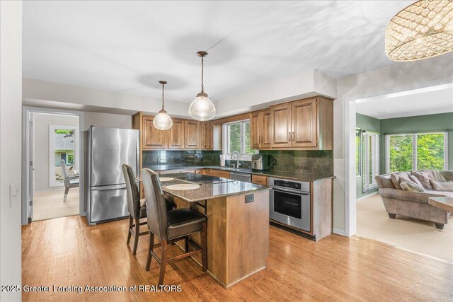 3886 Hemmingway Dr, Okemos, MI 48864 - kitchen with stainless steel appliances, decorative backsplash, a breakfast bar area, and light wood-style floors