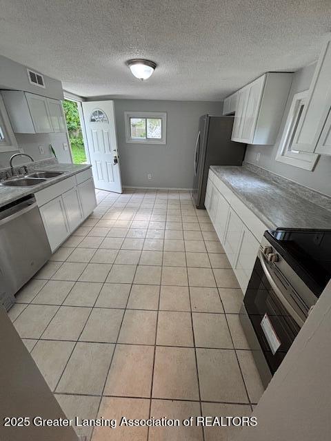 4013 Ingham St, Lansing, MI 48911 - kitchen with stainless steel appliances, white cabinets, light tile patterned floors, a textured ceiling, and light countertops