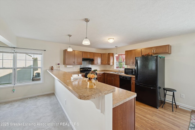 8687 Yellowstone Ln, Lansing, MI 48917 - kitchen with black appliances, a peninsula, light countertops, under cabinet range hood, and a kitchen bar