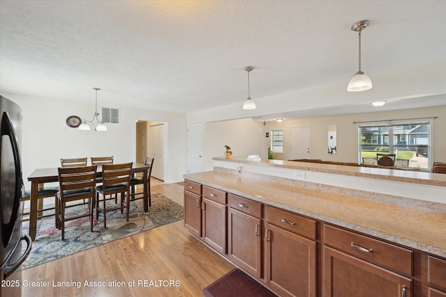 8687 Yellowstone Ln, Lansing, MI 48917 - kitchen with light wood-style flooring, freestanding refrigerator, pendant lighting, light countertops, and a textured ceiling