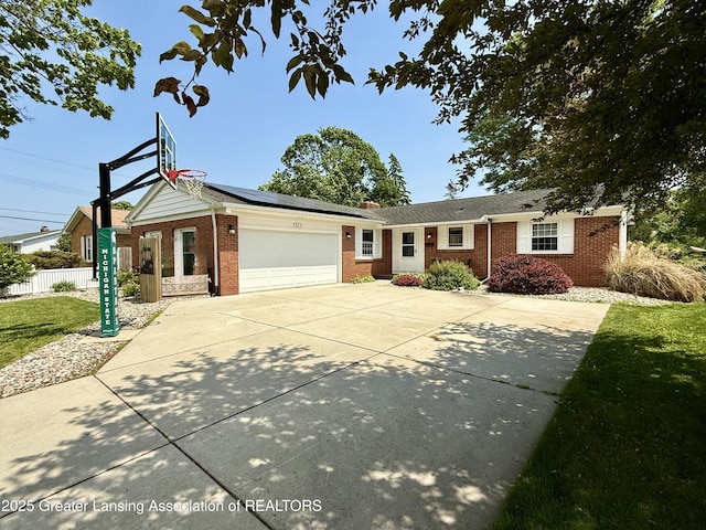 3321 Springbrook Ln, Lansing, MI 48917 - ranch-style house with brick siding, an attached garage, concrete driveway, and solar panels