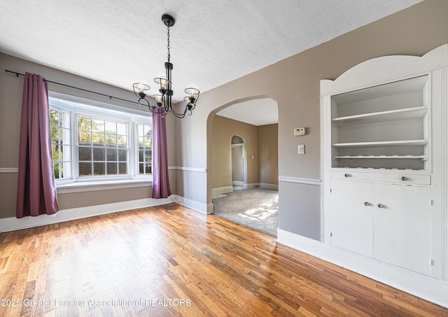 1407 W Ionia St, Lansing, MI 48915 - unfurnished dining area with a chandelier, arched walkways, light wood-style floors, and a textured ceiling