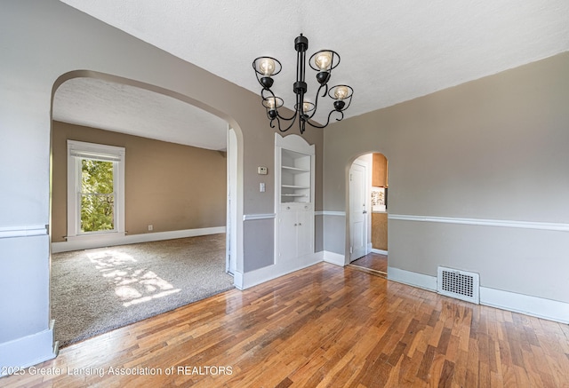1407 W Ionia St, Lansing, MI 48915 - unfurnished room featuring arched walkways, a chandelier, built in shelves, wood finished floors, and a textured ceiling
