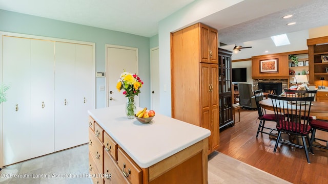 3522 Apple Valley Rd, Okemos, MI 48864 - kitchen with a lit fireplace, a skylight, a kitchen island, light wood finished floors, and recessed lighting