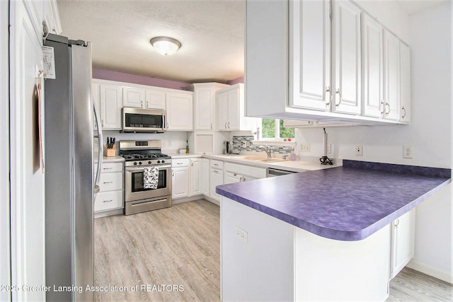 6093 Anchor Cv, Dimondale, MI 48821 - kitchen featuring stainless steel appliances, a peninsula, light wood-type flooring, dark countertops, and white cabinets