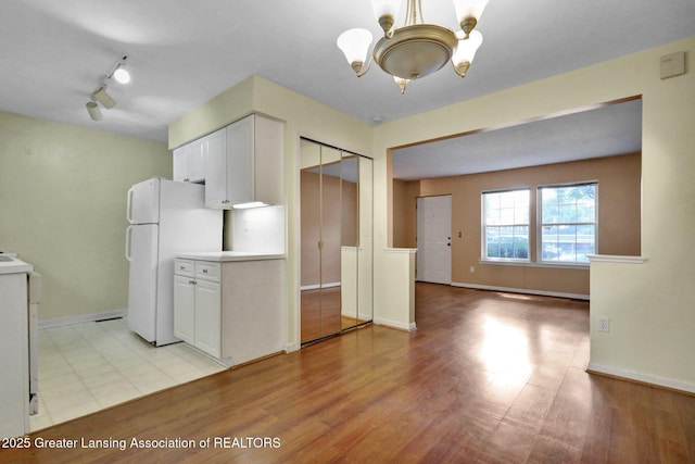 6213 Beechfield Dr, Lansing, MI 48911 - kitchen with freestanding refrigerator, a chandelier, white cabinetry, rail lighting, and light wood-type flooring