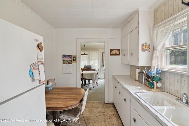 1213 N Woodworth Rd, Jackson, MI 49202 - kitchen featuring freestanding refrigerator, white cabinets, light countertops, wallpapered walls, and crown molding