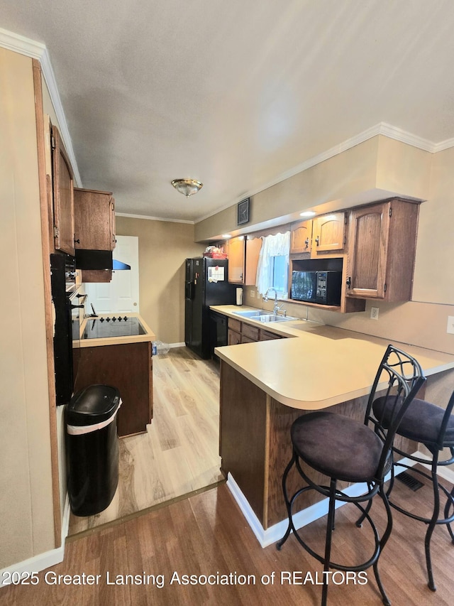 3701 Sumpter St, Lansing, MI 48911 - kitchen featuring black appliances, a peninsula, light wood finished floors, light countertops, and a kitchen bar