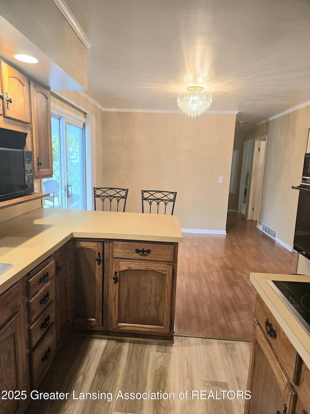 3701 Sumpter St, Lansing, MI 48911 - kitchen featuring black appliances, light countertops, a chandelier, a peninsula, and light wood-style floors