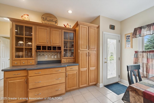 11195 Prestwick Dr, Lansing, MI 48917 - kitchen with light tile patterned floors, dark countertops, glass insert cabinets, brown cabinetry, and recessed lighting
