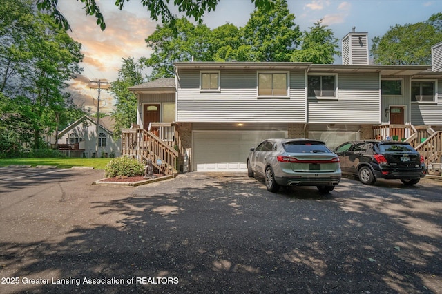 5041 E Willoughby Rd Unit 7, Holt, MI 48842 - view of front facade with a garage, asphalt driveway, a chimney, stairway, and brick siding