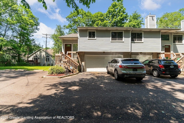 5041 E Willoughby Rd Unit 7, Holt, MI 48842 - view of front facade featuring an attached garage, stairs, brick siding, driveway, and a chimney