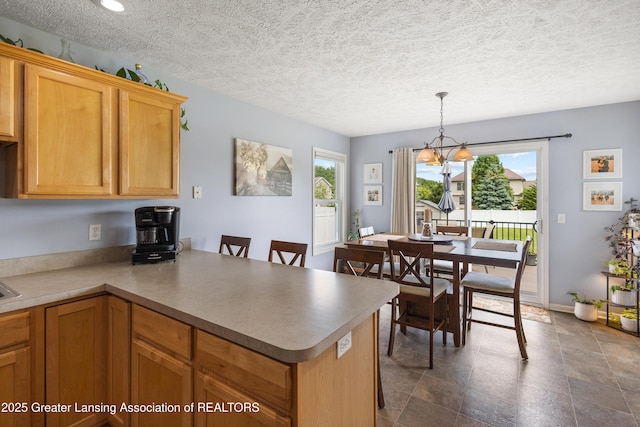 3913 Danbridge Dr, Lansing, MI 48906 - kitchen with a peninsula, a chandelier, a textured ceiling, hanging light fixtures, and light countertops