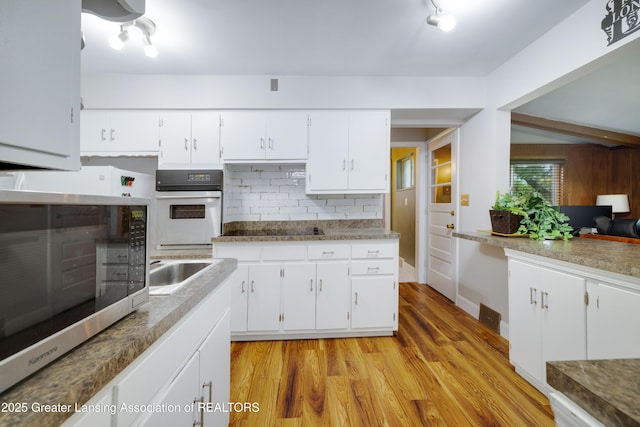 425 S Holmes St, Lansing, MI 48912 - kitchen featuring white oven, stainless steel microwave, light wood-style flooring, decorative backsplash, and white cabinets