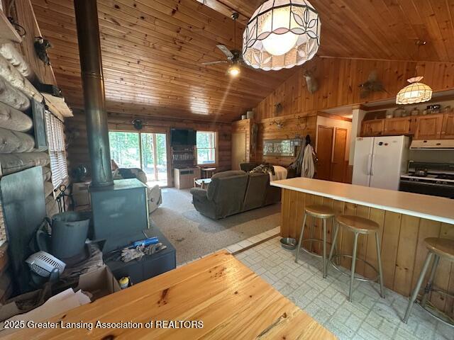 10886 SE Gillow Rd, Fife Lake, MI 49633 - living area featuring wooden ceiling, vaulted ceiling, a wood stove, wood walls, and light flooring