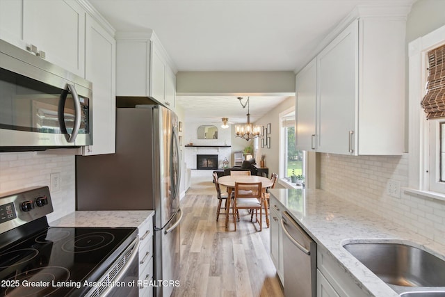 6244 Daft St, Lansing, MI 48911 - kitchen featuring stainless steel appliances, a glass covered fireplace, light wood-style floors, white cabinets, and backsplash