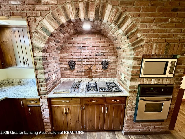 12830 Upton Rd, Bath, MI 48808 - kitchen with appliances with stainless steel finishes, light wood-style floors, brick wall, and light stone countertops