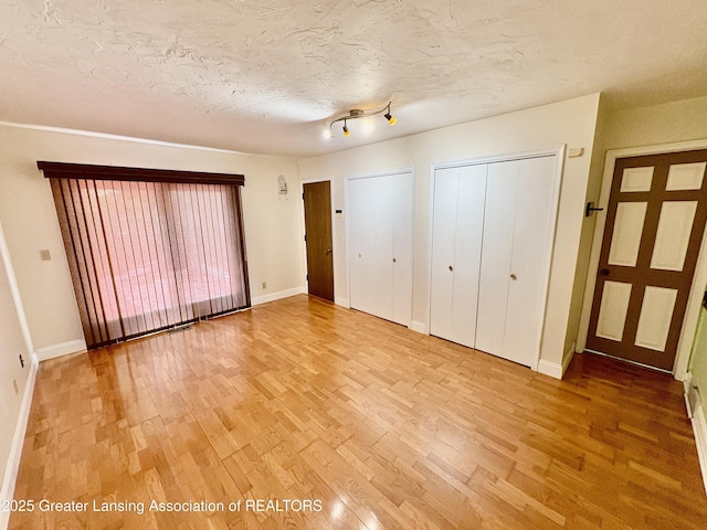 12830 Upton Rd, Bath, MI 48808 - unfurnished bedroom with light wood finished floors, two closets, and a textured ceiling