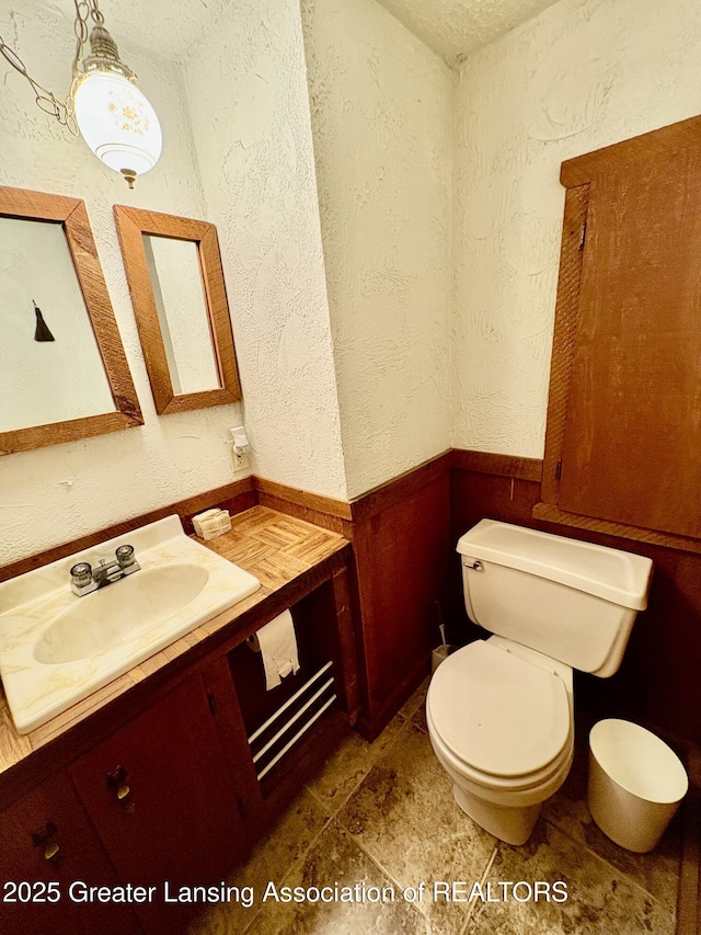 12830 Upton Rd, Bath, MI 48808 - bathroom with vanity, a textured wall, stone finish flooring, and wainscoting