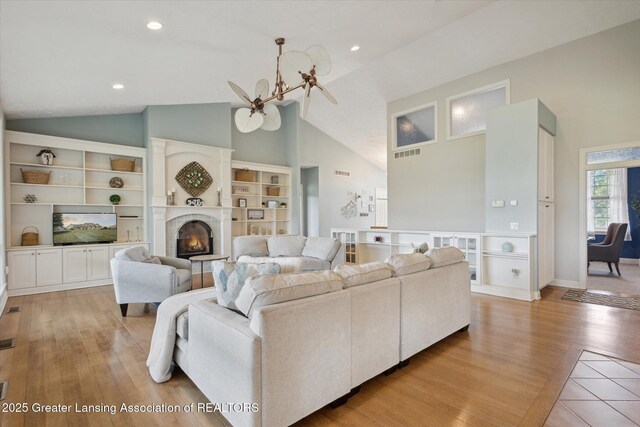5056 W Bunker Rd, Mason, MI 48854 - living room featuring light wood-style flooring, high vaulted ceiling, a lit fireplace, recessed lighting, and a chandelier