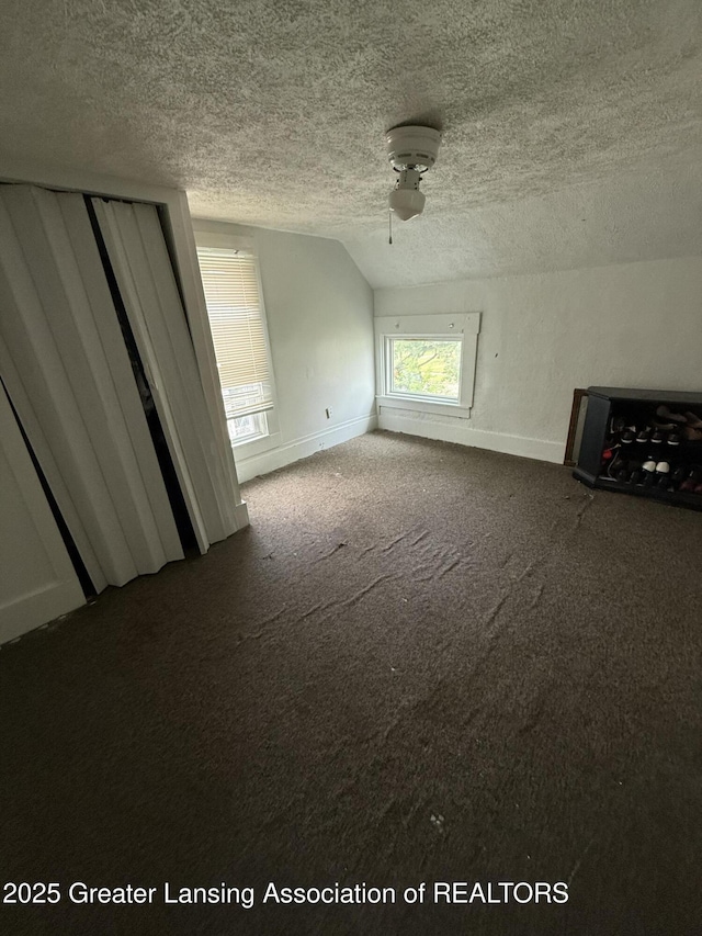 1018 E Kalamazoo St, Lansing, MI 48912 - unfurnished living room featuring a textured ceiling, dark colored carpet, vaulted ceiling, and ceiling fan