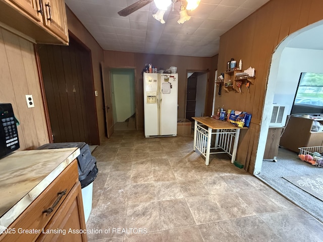 4317 S Cedar St, Lansing, MI 48910 - kitchen with white fridge with ice dispenser, arched walkways, a ceiling fan, brown cabinets, and wood walls