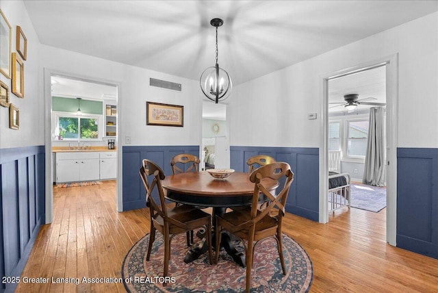 520 Wood St, Eaton Rapids, MI 48827 - dining space featuring light wood finished floors, wainscoting, a ceiling fan, a chandelier, and a decorative wall