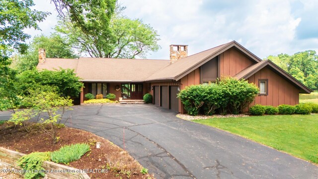 280 Winterberry Ln, Okemos, MI 48864 - view of front of house with board and batten siding, a chimney, driveway, and an attached garage