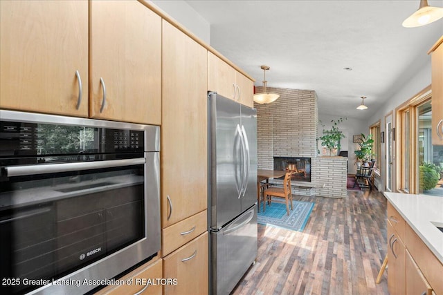10138 Baron Blvd, Dimondale, MI 48821 - kitchen with appliances with stainless steel finishes, light brown cabinets, wood finished floors, a fireplace, and pendant lighting