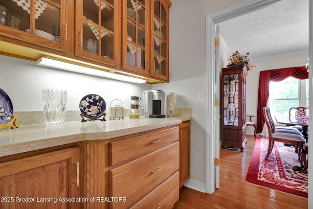 1823 Cricket Ln, East Lansing, MI 48823 - kitchen with brown cabinets, glass insert cabinets, wood finished floors, ornamental molding, and a textured ceiling