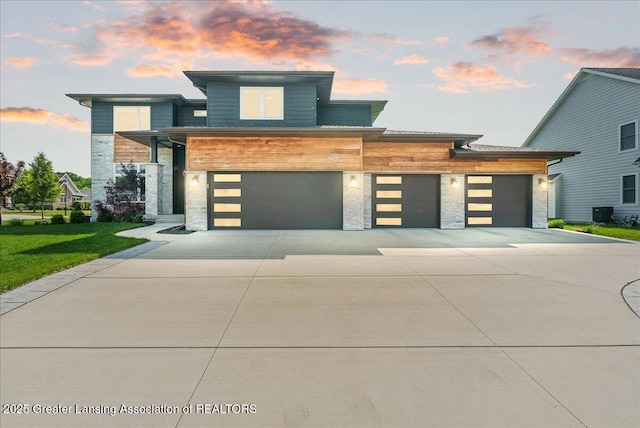 6102 Sleepy Hollow Ln, East Lansing, MI 48823 - modern home featuring stone siding, concrete driveway, a garage, and a lawn
