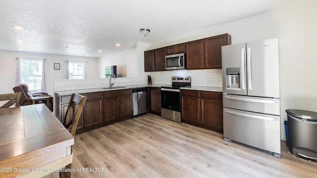 1118 River Oaks Dr, Dewitt, MI 48820 - kitchen with stainless steel appliances, dark brown cabinetry, light wood-type flooring, decorative backsplash, and light stone counters