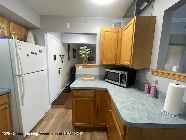 5535 W St Joe Hwy Unit B12, Lansing, MI 48917 - kitchen featuring freestanding refrigerator, stainless steel microwave, light wood-style floors, brown cabinetry, and light countertops