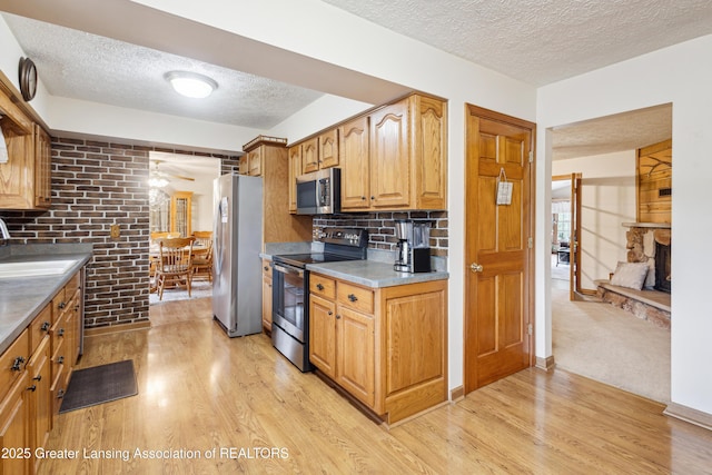 888 S Waverly Rd, Eaton Rapids, MI 48827 - kitchen featuring stainless steel appliances, a textured ceiling, light wood-style floors, a stone fireplace, and tasteful backsplash