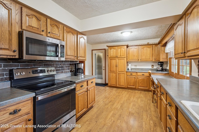 888 S Waverly Rd, Eaton Rapids, MI 48827 - kitchen with stainless steel appliances, a textured ceiling, light wood finished floors, brown cabinets, and decorative backsplash