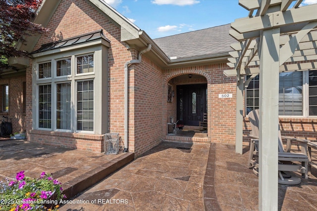 502 W Spring Meadows Ln, Dewitt, MI 48820 - property entrance featuring a shingled roof, brick siding, and a patio area