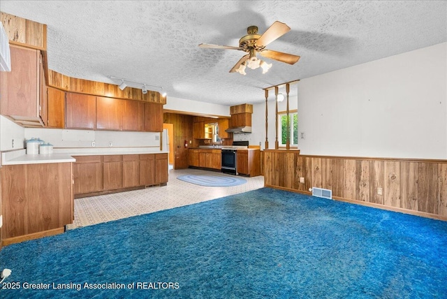 952 Leslie St, Lansing, MI 48912 - kitchen featuring brown cabinets, open floor plan, wood walls, ceiling fan, and a textured ceiling