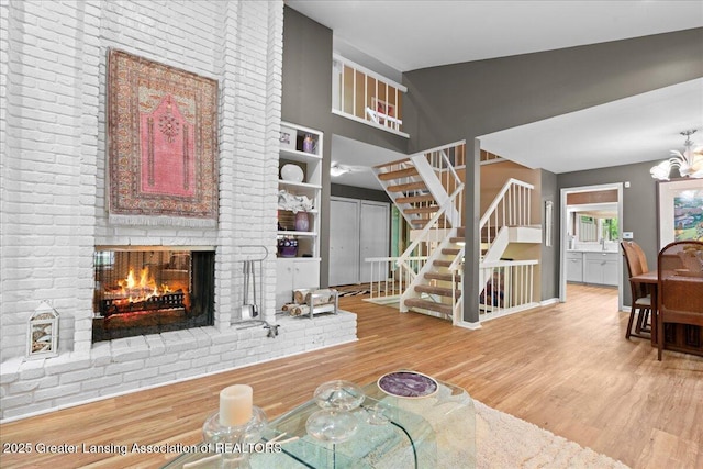 1122 Farwood Dr, East Lansing, MI 48823 - living area featuring wood finished floors, a brick fireplace, stairs, vaulted ceiling, and a chandelier